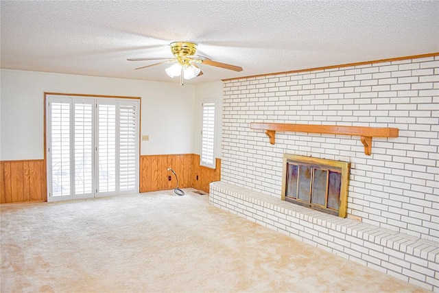 unfurnished living room with a brick fireplace, carpet, a textured ceiling, and wood walls