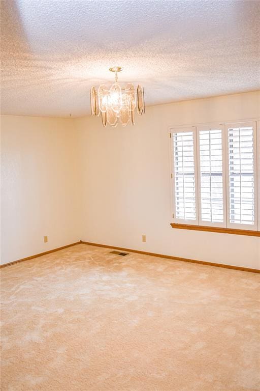 spare room featuring an inviting chandelier, carpet flooring, and a textured ceiling