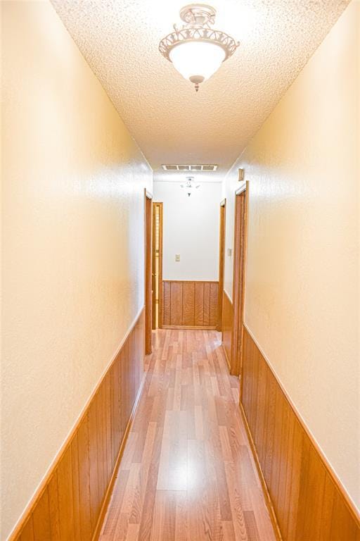 hall featuring light hardwood / wood-style flooring, a textured ceiling, and wood walls