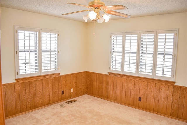 spare room with ceiling fan, light colored carpet, a textured ceiling, and wooden walls