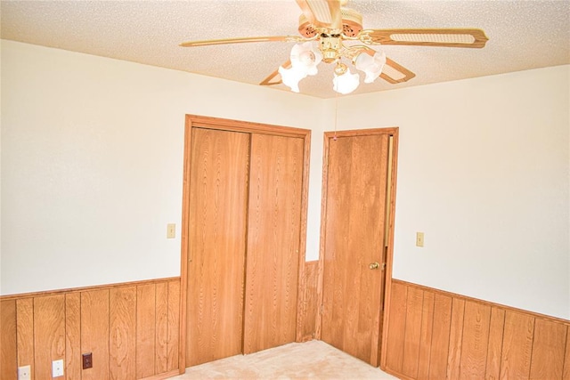 unfurnished bedroom with a closet, carpet, a textured ceiling, and wood walls