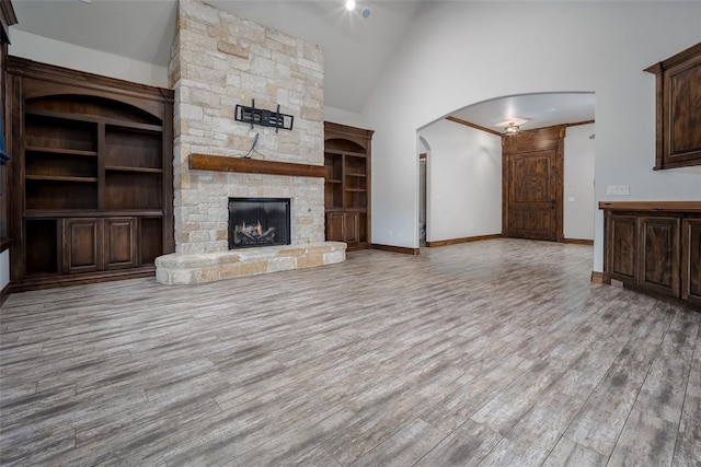 unfurnished living room with a stone fireplace, high vaulted ceiling, and light wood-type flooring