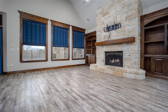 unfurnished living room featuring built in shelves, a fireplace, high vaulted ceiling, and light wood-type flooring