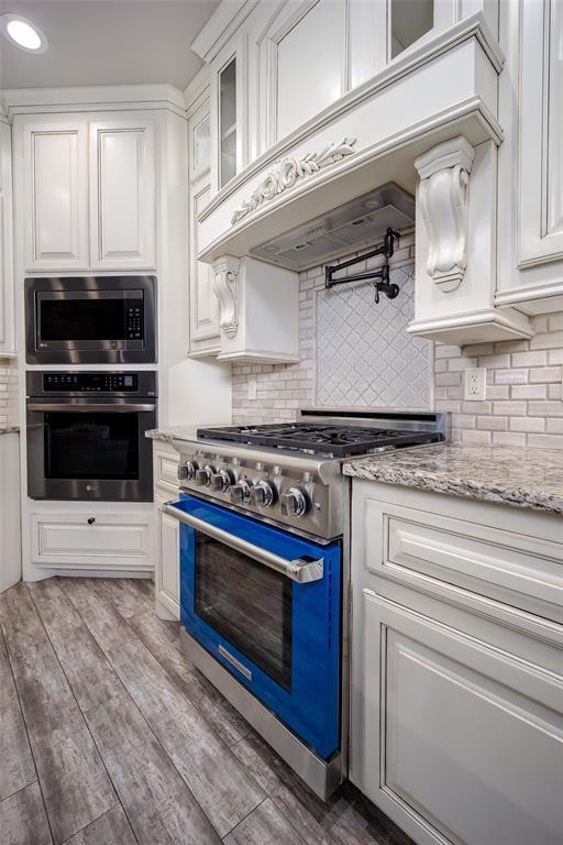 kitchen with appliances with stainless steel finishes, white cabinetry, backsplash, light hardwood / wood-style floors, and custom range hood