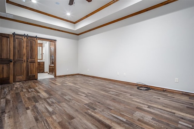 unfurnished bedroom featuring hardwood / wood-style floors, crown molding, ensuite bath, and a barn door