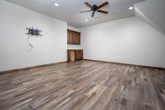 unfurnished living room featuring ceiling fan, dark hardwood / wood-style flooring, built in desk, and vaulted ceiling