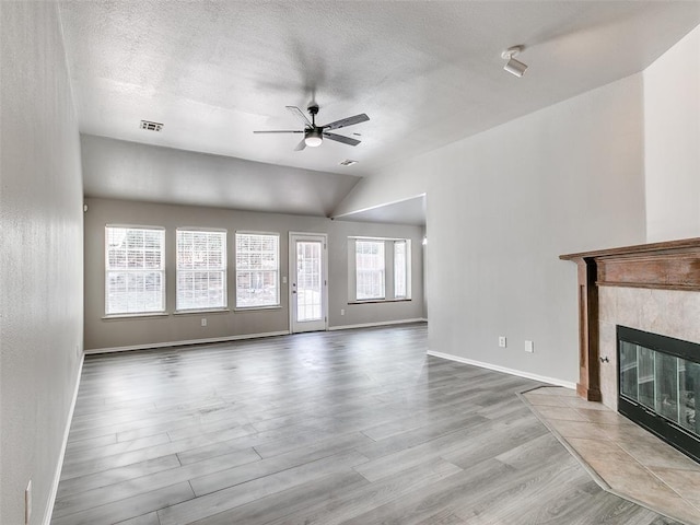 unfurnished living room with vaulted ceiling, a textured ceiling, light wood-type flooring, ceiling fan, and a tiled fireplace