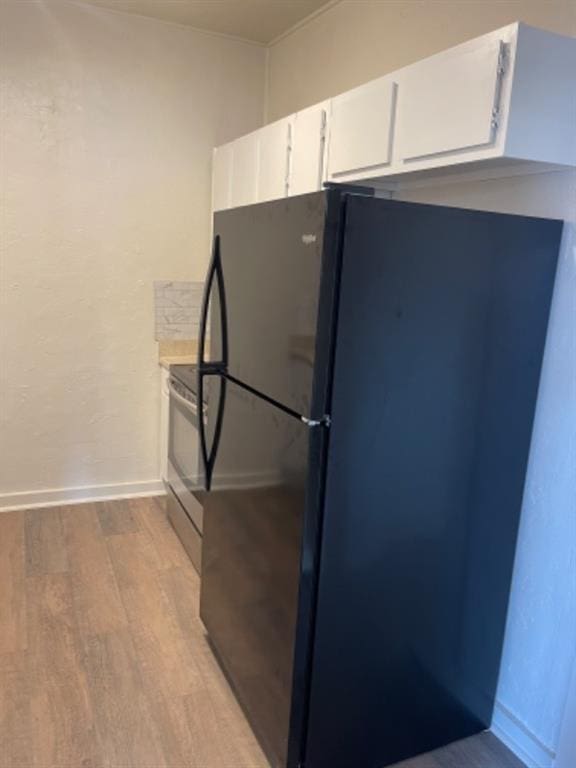 kitchen with white cabinetry, black fridge, electric range, and light wood-type flooring