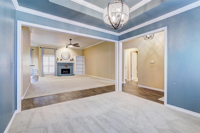 unfurnished living room featuring ornamental molding, a brick fireplace, carpet flooring, and ceiling fan with notable chandelier