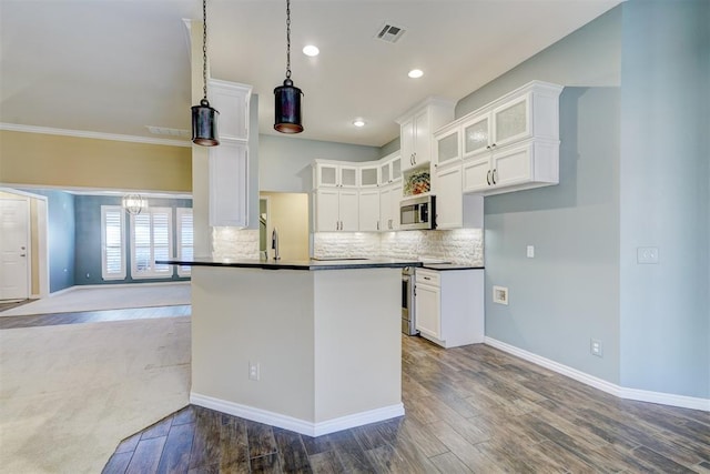 kitchen featuring appliances with stainless steel finishes, pendant lighting, white cabinets, hardwood / wood-style flooring, and kitchen peninsula