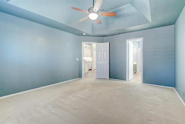 unfurnished bedroom featuring light carpet, a tray ceiling, ceiling fan, and ensuite bathroom