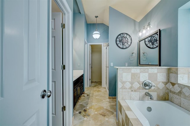 bathroom with vanity, tiled tub, and lofted ceiling