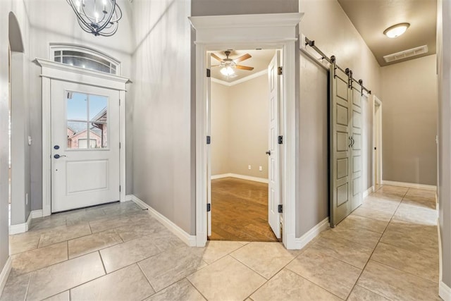 tiled entrance foyer with ornamental molding, a barn door, and ceiling fan