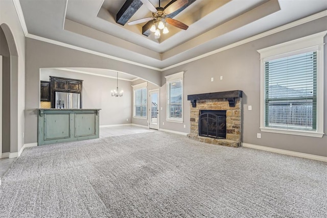 unfurnished living room with a tray ceiling, a stone fireplace, ceiling fan with notable chandelier, and light carpet