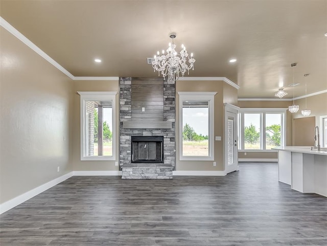 unfurnished living room with ornamental molding, a stone fireplace, dark wood-type flooring, and an inviting chandelier