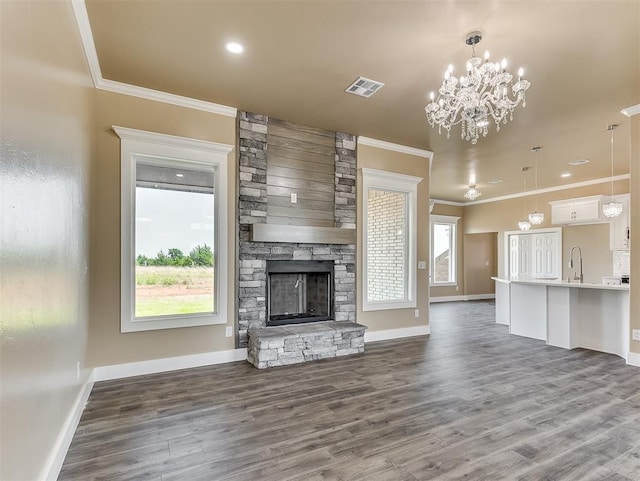 unfurnished living room with a fireplace, sink, a chandelier, ornamental molding, and dark wood-type flooring