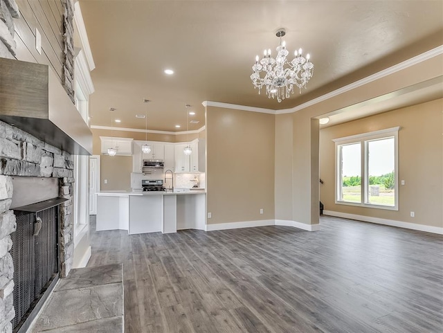 unfurnished living room featuring sink, crown molding, dark wood-type flooring, a fireplace, and a chandelier