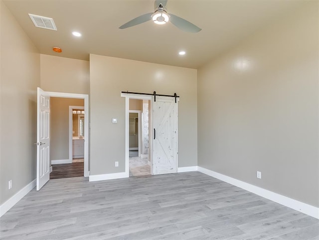 unfurnished bedroom with a barn door, ceiling fan, and light wood-type flooring