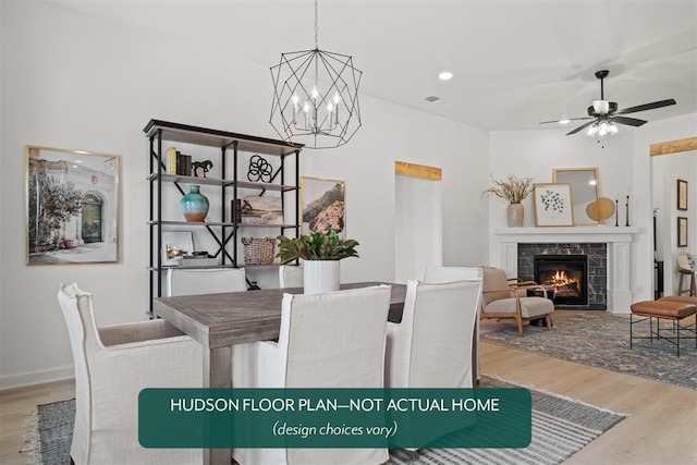 dining room featuring hardwood / wood-style flooring, a tiled fireplace, and ceiling fan with notable chandelier