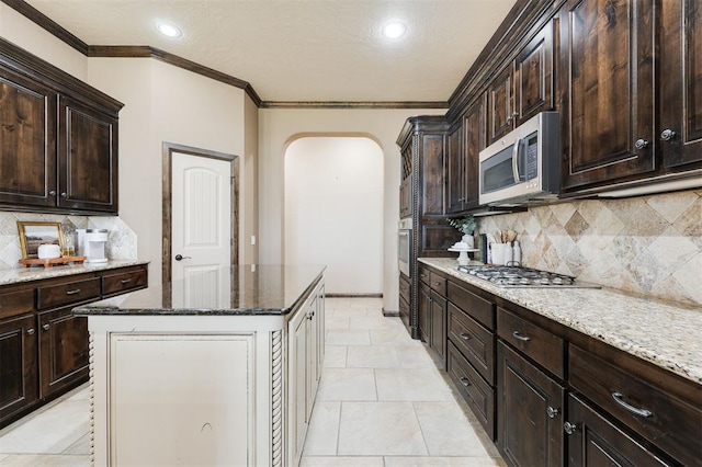 kitchen with dark brown cabinets, stainless steel appliances, dark stone counters, and a kitchen island