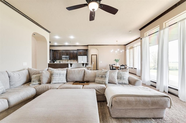 carpeted living room featuring ornamental molding, ceiling fan with notable chandelier, and a baseboard heating unit