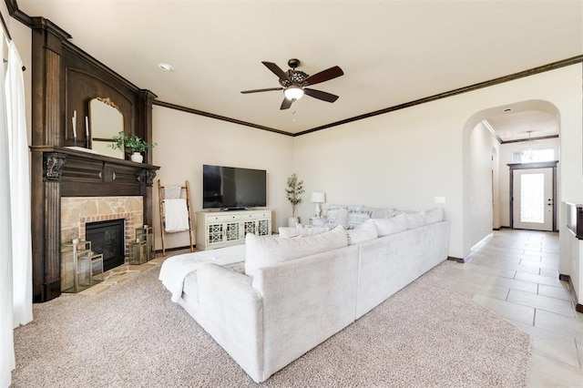 living room featuring light tile patterned flooring, a stone fireplace, crown molding, and ceiling fan