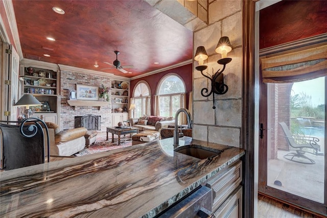 kitchen featuring sink, built in features, ceiling fan, ornamental molding, and a brick fireplace