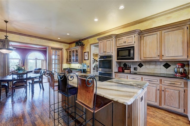 kitchen with hanging light fixtures, black appliances, a kitchen island, decorative backsplash, and light wood-type flooring