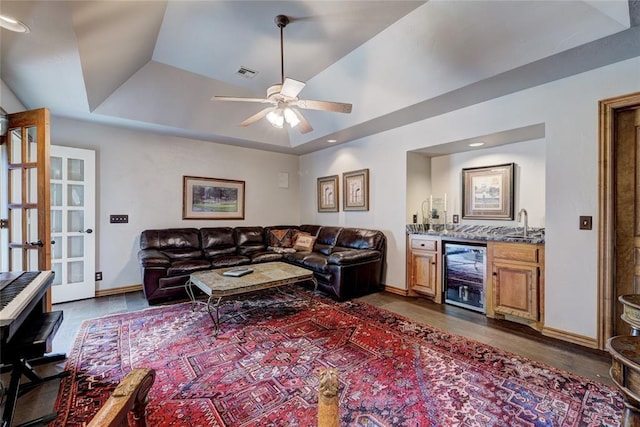 living room with ceiling fan, dark hardwood / wood-style floors, wine cooler, bar area, and a raised ceiling