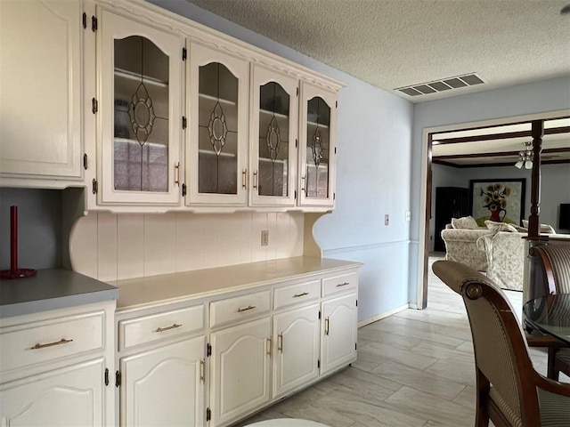 kitchen with visible vents, glass insert cabinets, light countertops, a textured ceiling, and white cabinetry