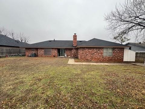 rear view of property featuring fence, a lawn, and brick siding