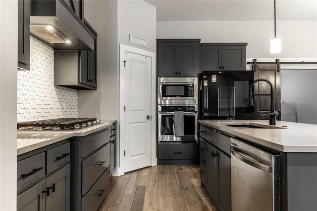 kitchen featuring appliances with stainless steel finishes, sink, dark hardwood / wood-style flooring, hanging light fixtures, and wall chimney exhaust hood