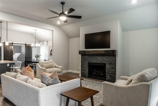 living room featuring ceiling fan with notable chandelier, a fireplace, wood-type flooring, lofted ceiling, and a barn door