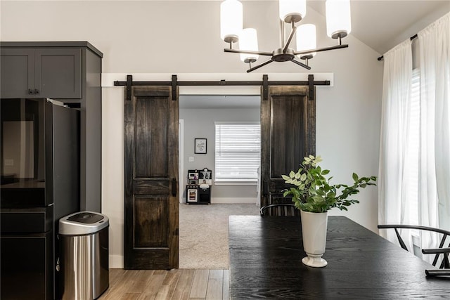 dining space with an inviting chandelier, lofted ceiling, a barn door, and light hardwood / wood-style flooring