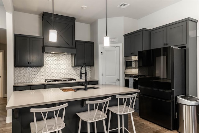 kitchen with stainless steel appliances, a kitchen island with sink, and decorative light fixtures