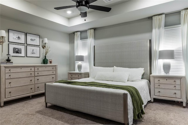 bedroom featuring ceiling fan, a tray ceiling, and light carpet