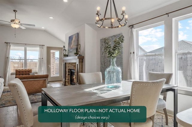 dining room featuring ceiling fan with notable chandelier, plenty of natural light, a fireplace, and vaulted ceiling