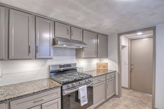 kitchen featuring gray cabinetry, decorative backsplash, stainless steel gas range, and dark stone counters