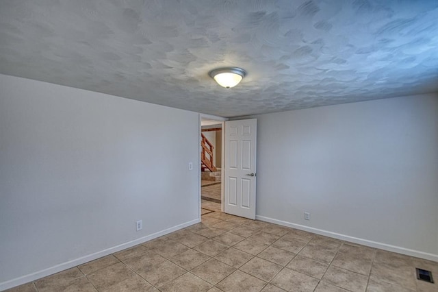 tiled empty room featuring a textured ceiling