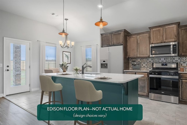 kitchen featuring appliances with stainless steel finishes, decorative light fixtures, sink, dark brown cabinetry, and a center island with sink