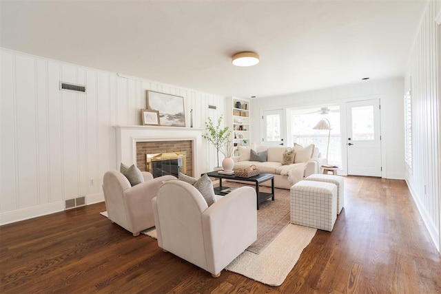 living room with a brick fireplace, built in features, and dark hardwood / wood-style flooring