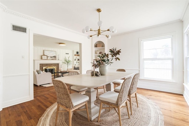 dining area featuring hardwood / wood-style floors, built in features, a fireplace, crown molding, and an inviting chandelier