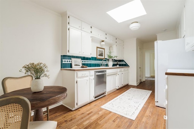 kitchen featuring white cabinetry, a skylight, light wood-type flooring, white refrigerator, and backsplash