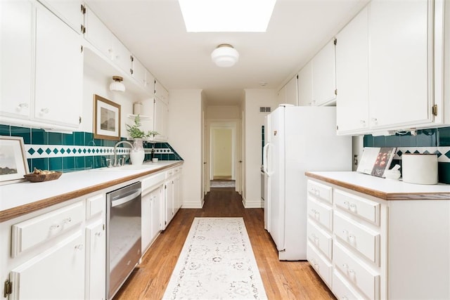 kitchen with a skylight, dishwasher, sink, white cabinets, and white fridge