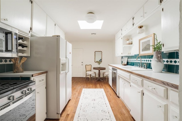 kitchen with sink, light hardwood / wood-style flooring, appliances with stainless steel finishes, a skylight, and white cabinets