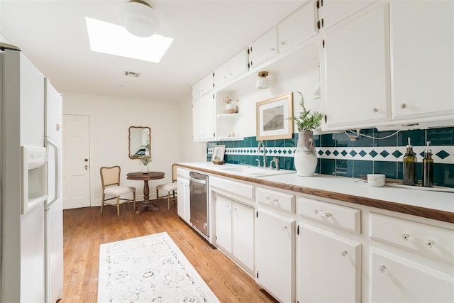 kitchen with tasteful backsplash, a skylight, stainless steel dishwasher, white refrigerator with ice dispenser, and white cabinets