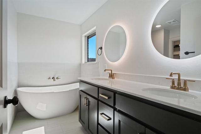 bathroom featuring visible vents, a sink, tile walls, and a freestanding bath