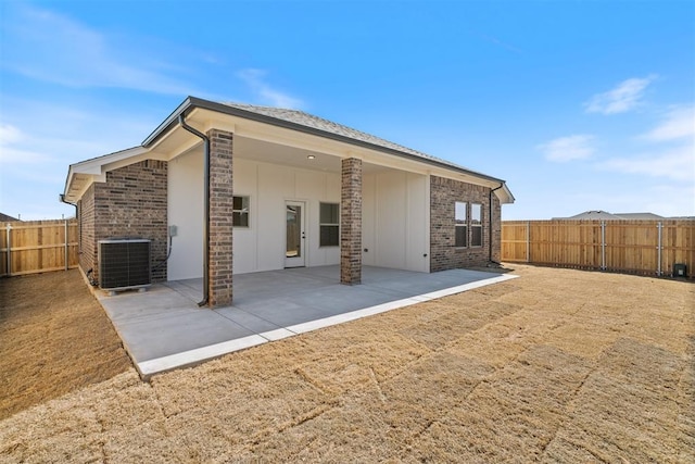 back of property with a fenced backyard, central air condition unit, brick siding, board and batten siding, and a patio area