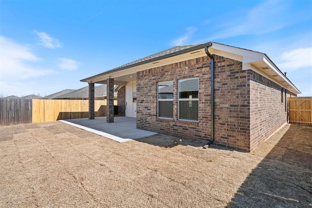 view of side of property with brick siding, a patio area, and a fenced backyard