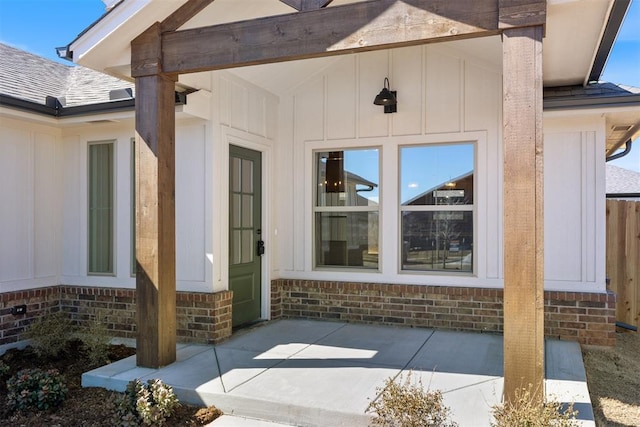 doorway to property with board and batten siding, a patio area, brick siding, and a shingled roof